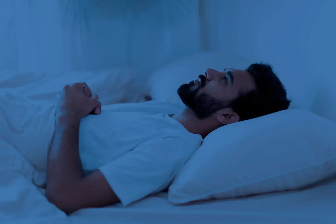 Man lying awake in bed at night, appearing sleep-deprived and restless